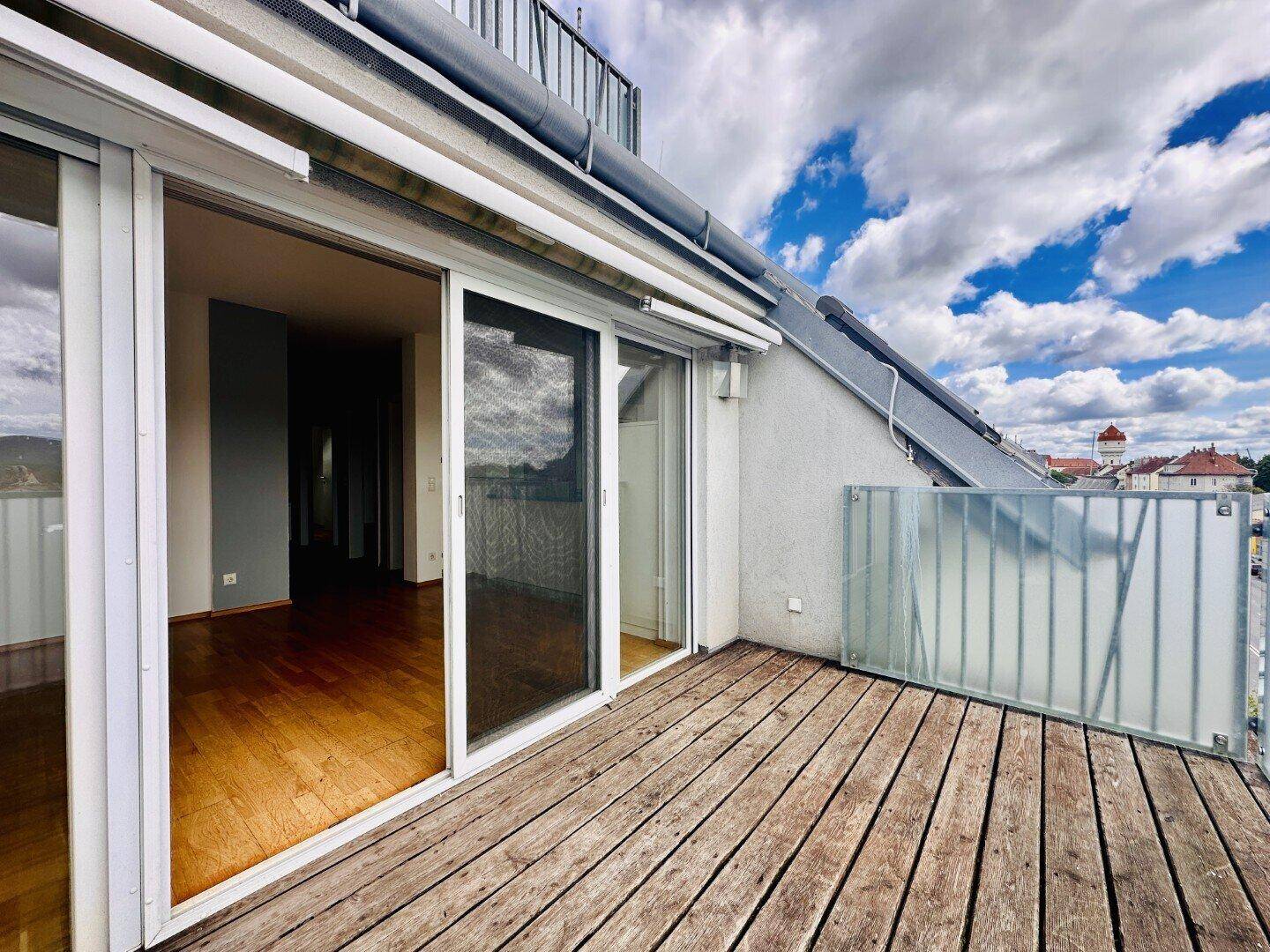 Geräumige Dachterrasse mit Holzboden und Stadtblick unter blauem Himmel.