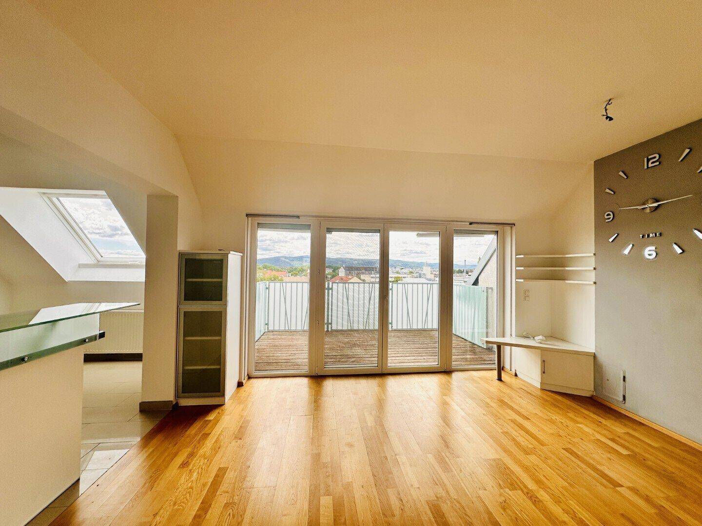 Helles Wohnzimmer mit Holzboden, Dachfenster und Zugang zu einer großen Dachterrasse.