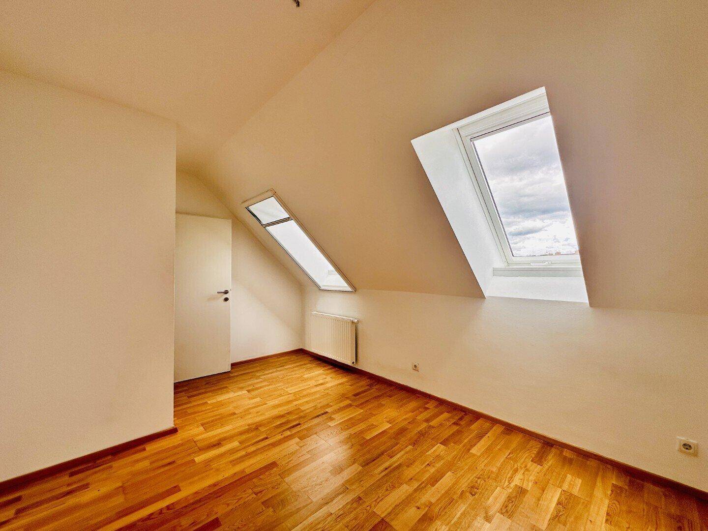 Helles Schlafzimmer im Dachgeschoss mit Holzboden und zwei Dachfenstern.