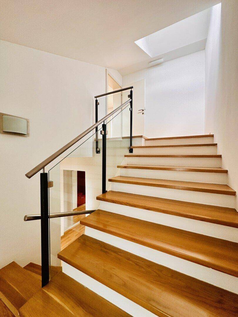 Elegante Holztreppe mit Glasgeländer und natürlichem Lichteinfall von oben.