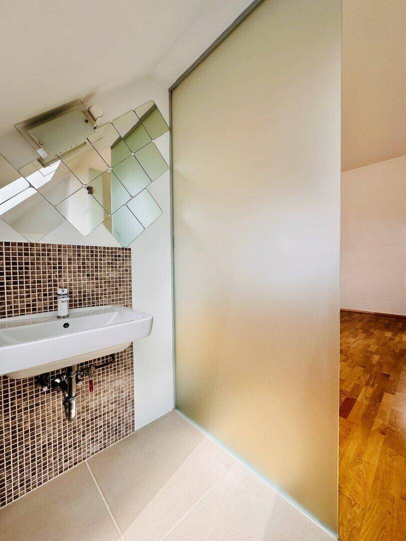 Kleines WC mit Waschbecken, Mosaikfliesen und Milchglastür.