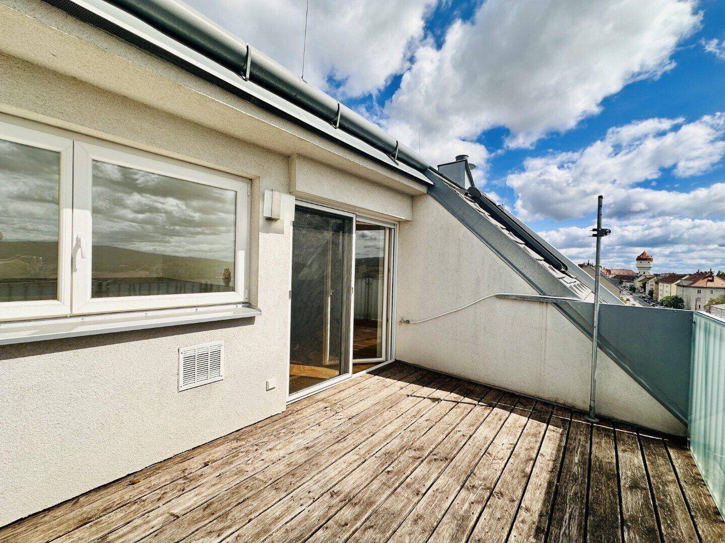 Dachterrasse mit Holzboden und Blick auf die Umgebung unter bewölktem Himmel.