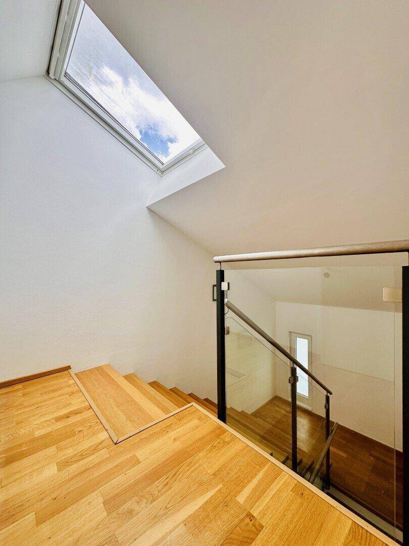 Heller Treppenabsatz mit Holzboden, Glasgeländer und Dachfenster für natürliches Licht.