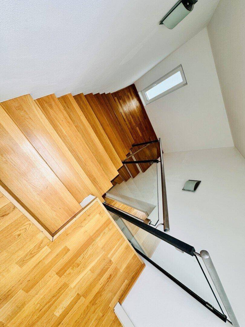 Moderne Holztreppe mit Glasgeländer und natürlichem Lichteinfall von oben.