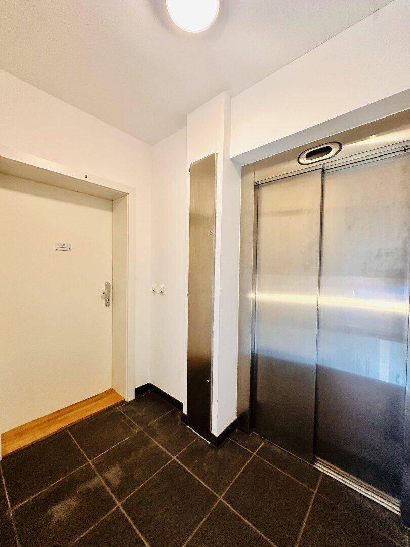 Eingangsbereich mit Aufzug und dunklem Fliesenboden.