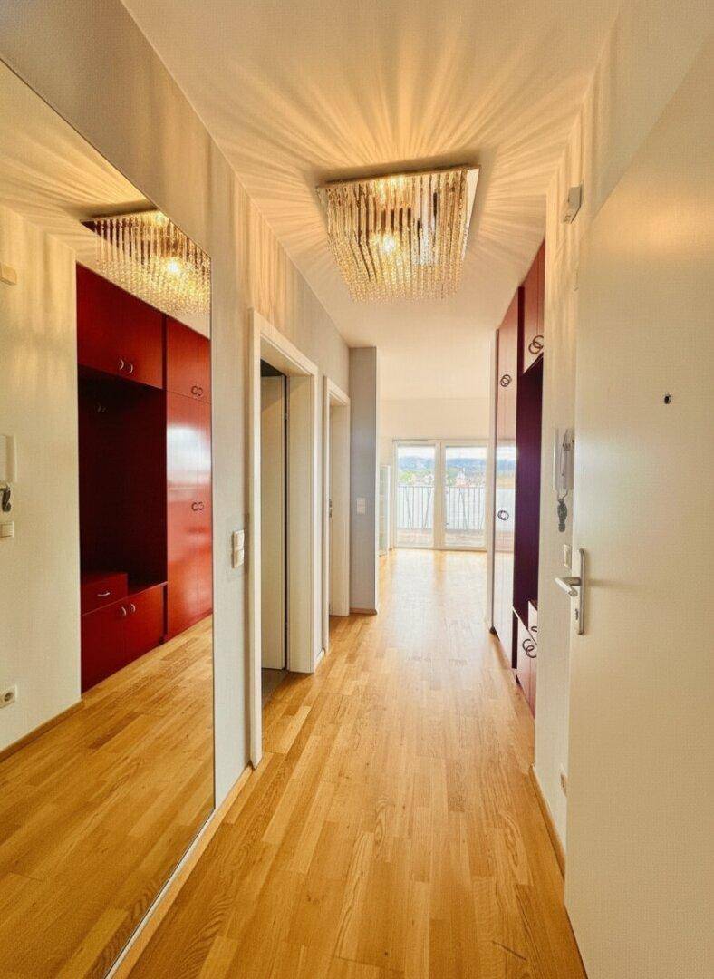 Heller Flur mit Holzboden, roten Einbauschränken und Spiegelfläche.