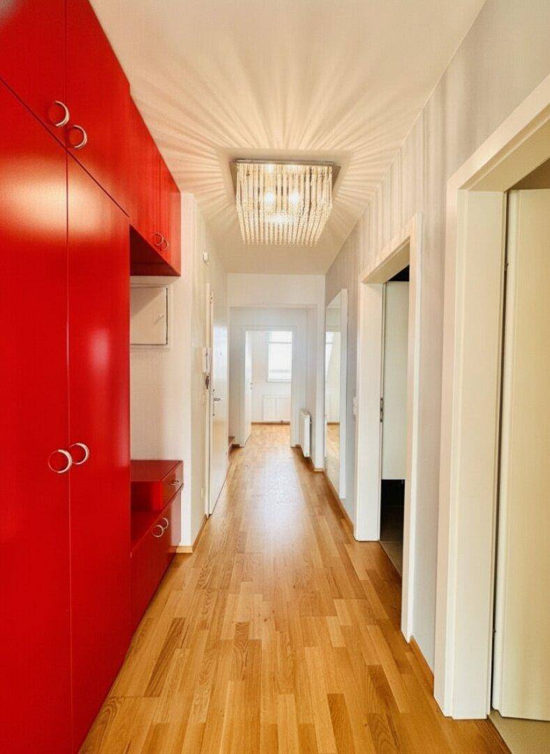 Langer Flur mit Holzboden, roten Einbauschränken und moderner Deckenleuchte.
