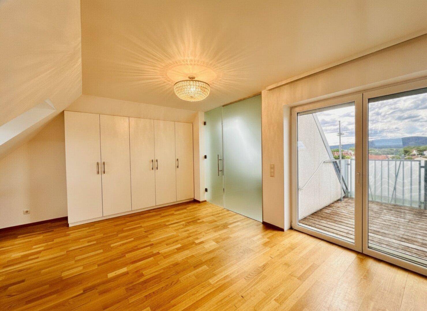Helles Schlafzimmer im Dachgeschoss mit Einbauschränken, Holzboden und Zugang zur Dachterrasse.