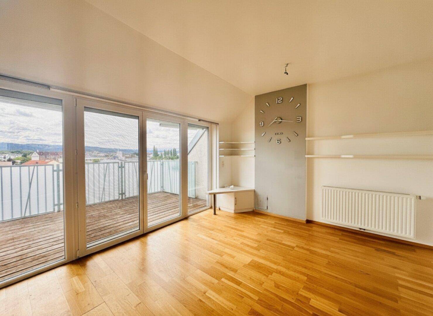 Geräumiges Wohnzimmer mit Holzboden, großer Fensterfront und Zugang zur Dachterrasse mit Stadtblick.
