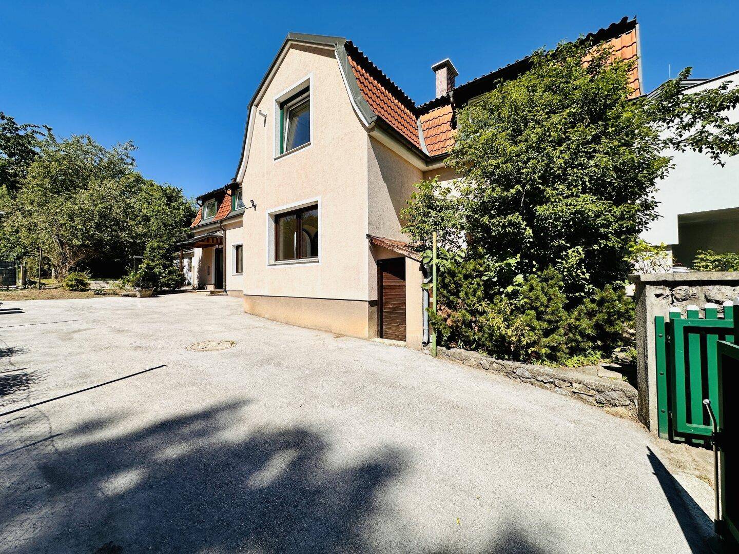 Seitenansicht des Hauses mit weitläufiger Auffahrt und grüner Bepflanzung.