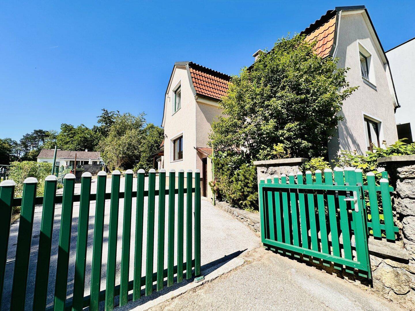 Ansicht des Hauses von der Straße mit grünem Tor und gepflegter Außenanlage.