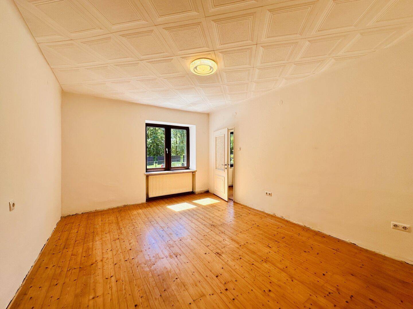 Helles Zimmer mit neu verlegten Holzplankenböden, Fenster und strukturierter Decke.