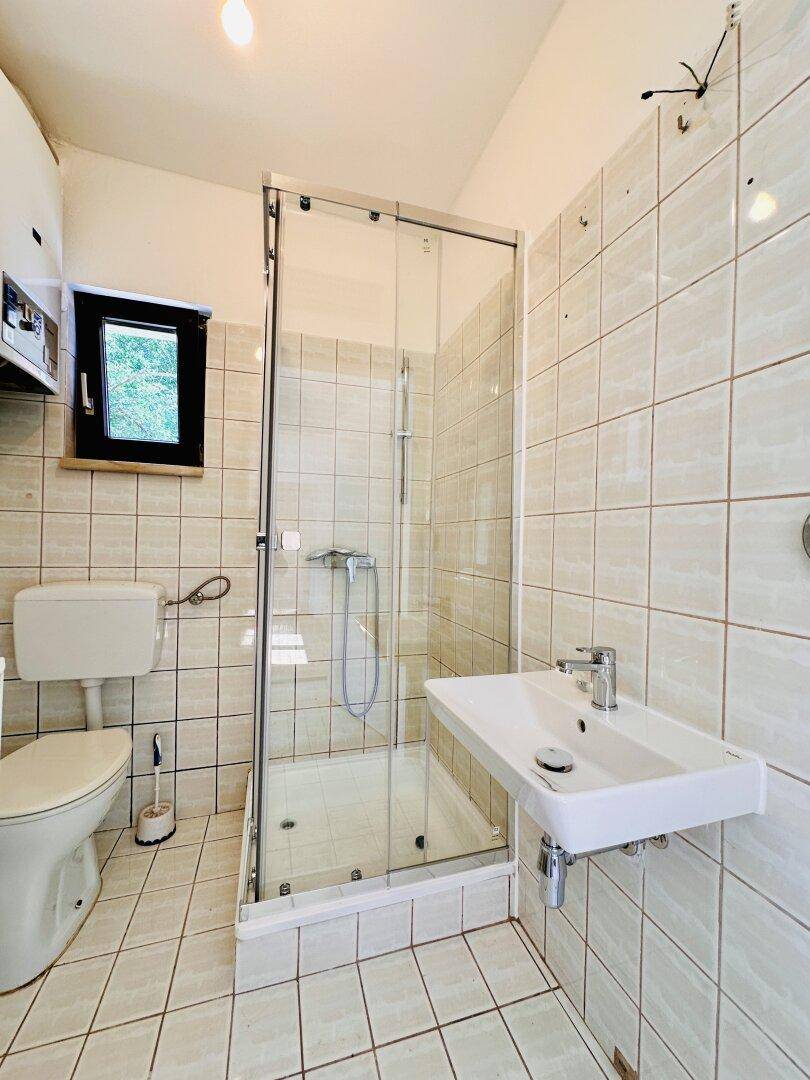 Kleines Badezimmer mit Duschkabine, Toilette, Waschbecken und hellen Fliesen.