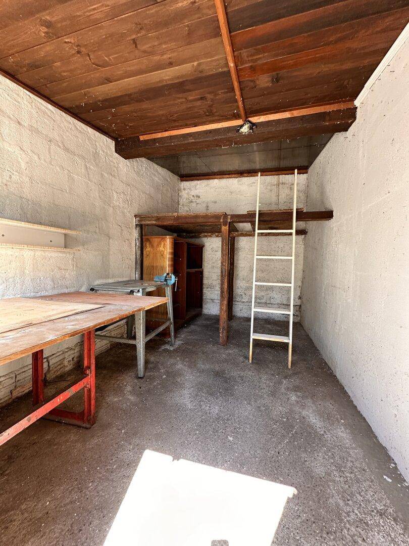 Rustikaler Werkstattraum mit Betonboden, Holzbalkendecke und einer Leiter zu einem Hochbett.