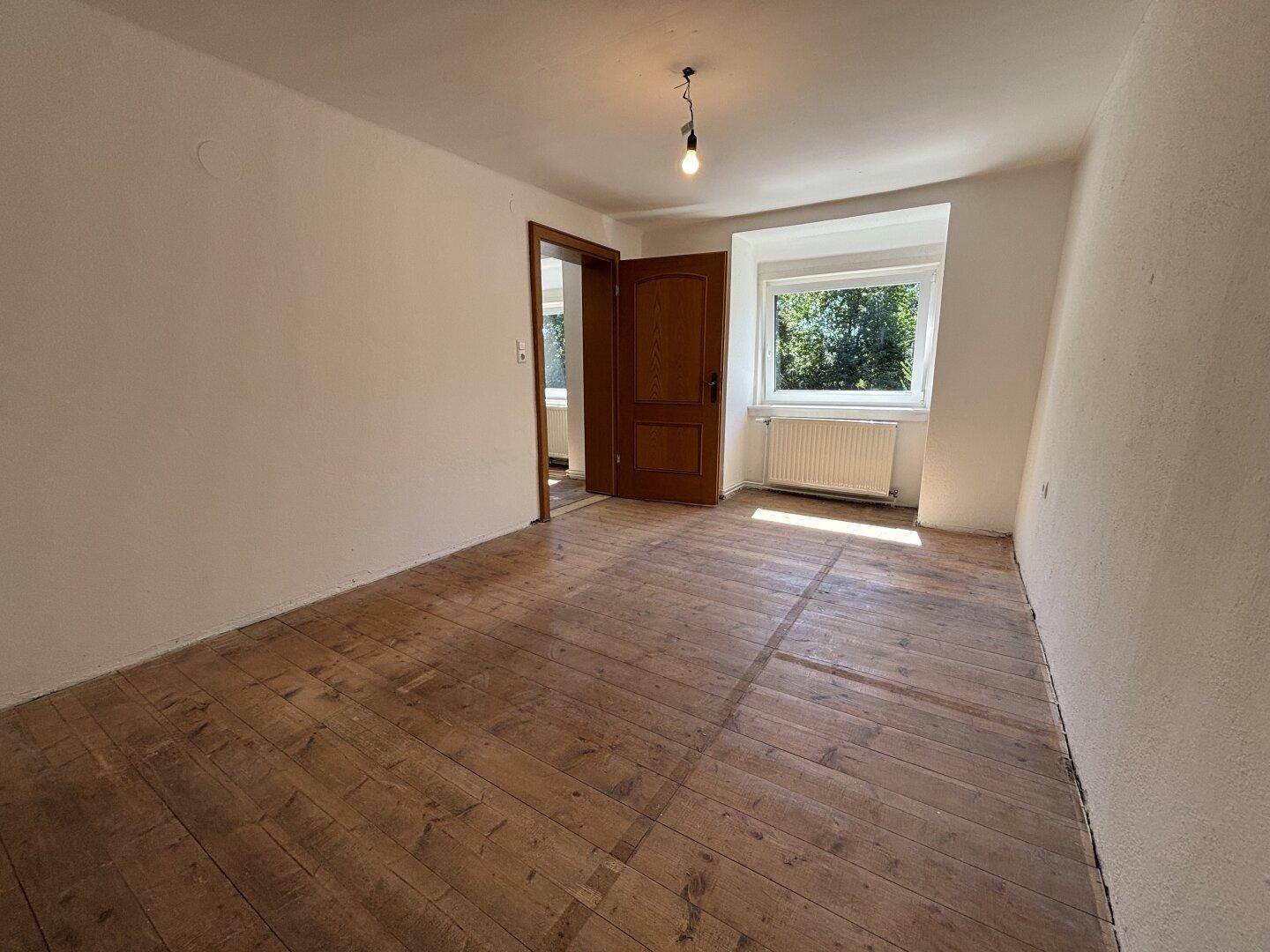 Leeres Schlafzimmer mit freigelegten Dielenböden und Fenster mit Blick ins Grüne.