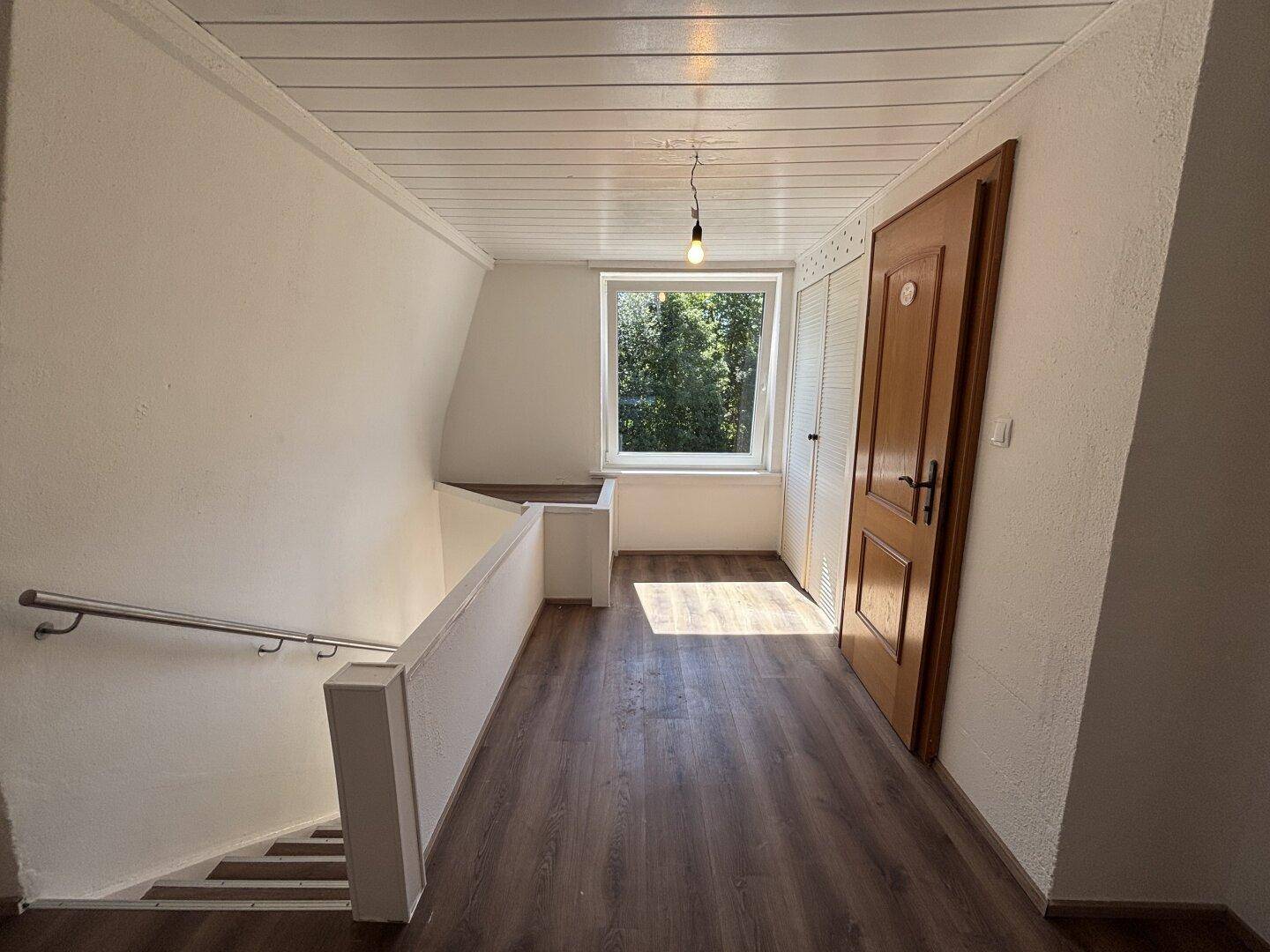 Obergeschoss-Flur mit Laminatboden, Holzdecke und Fenster mit Blick ins Grüne.