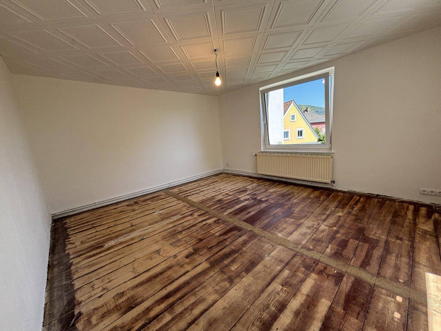 Leeres Zimmer mit freigelegten Dielenböden, Fenster und strukturierter Decke, ideal zur Renovierung.