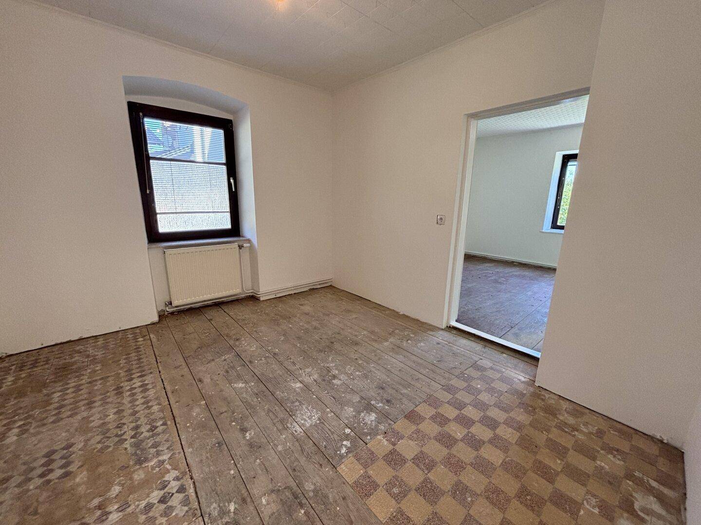 Zimmer mit freigelegten Dielenböden und einem Fenster, das viel Tageslicht hereinlässt.