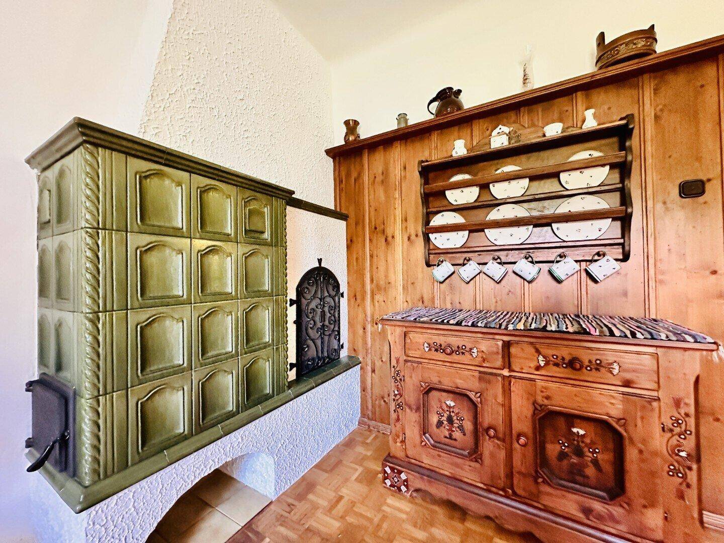 Detailansicht eines grünen Kachelofens und eines verzierten Holzschranks.