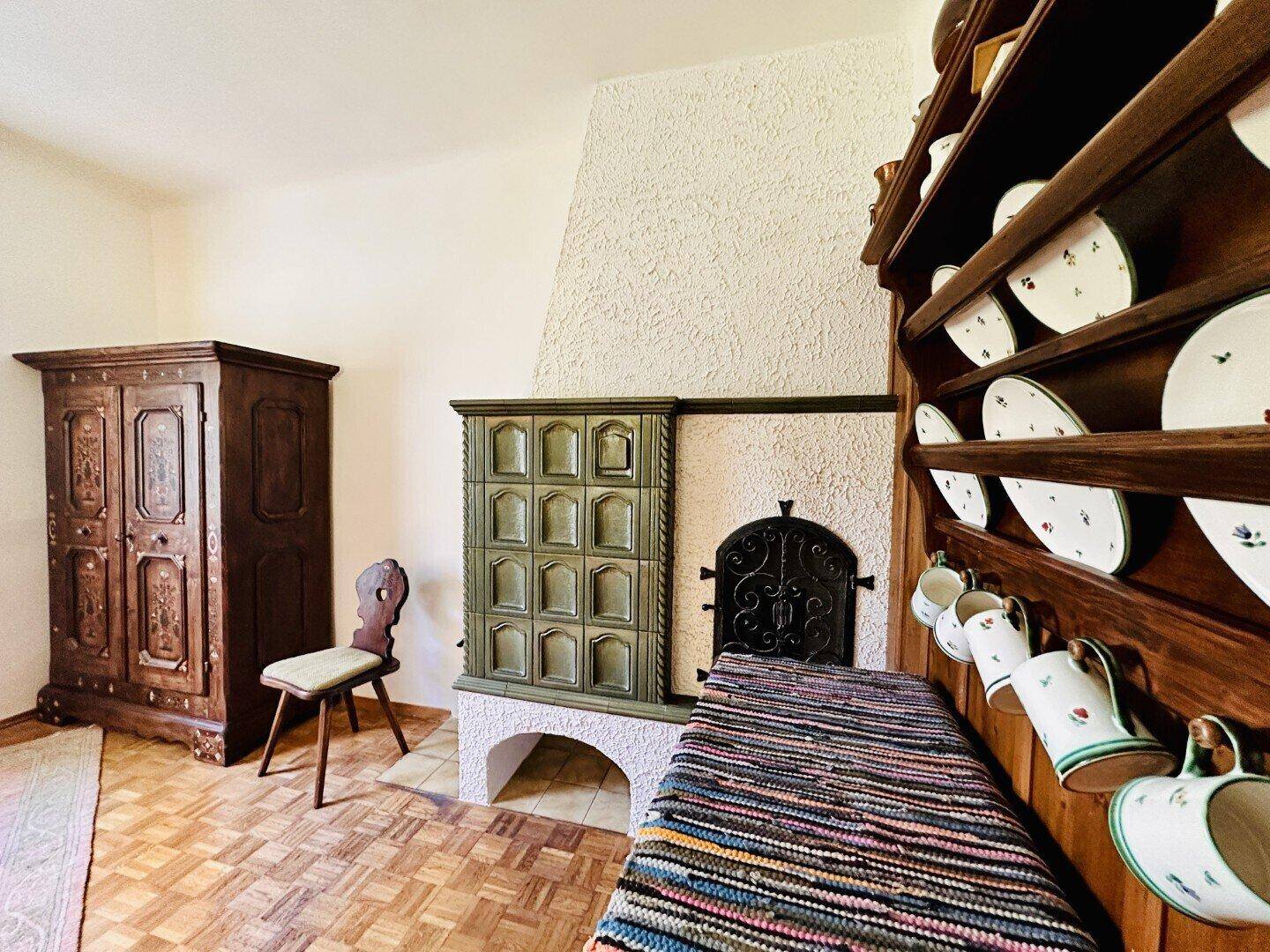 Gemütlicher Essbereich mit Kachelofen, Holzboden und traditionellem Schrank.