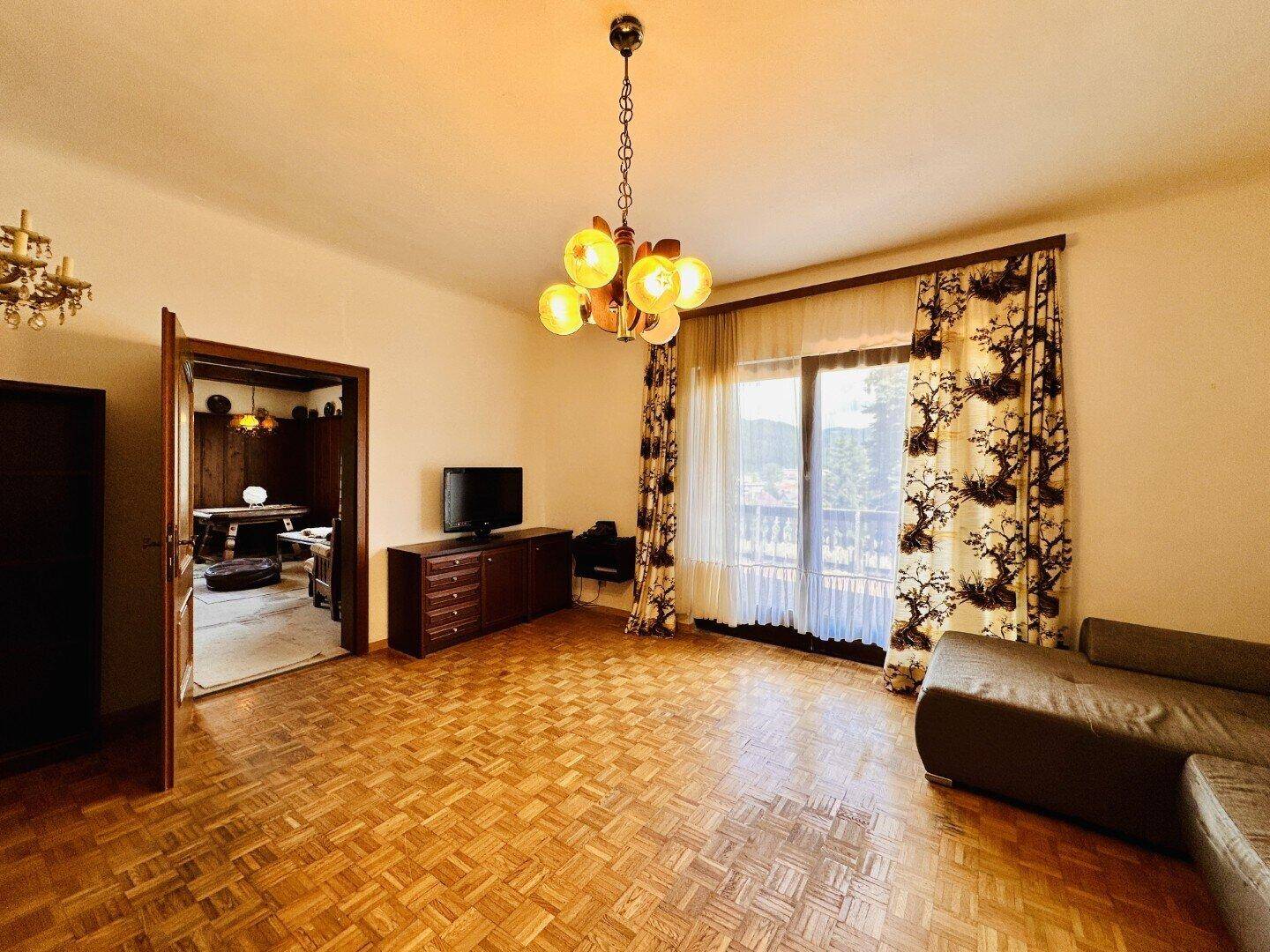Helles Wohnzimmer mit Parkettboden, Zugang zum Balkon und Blick ins Grüne.