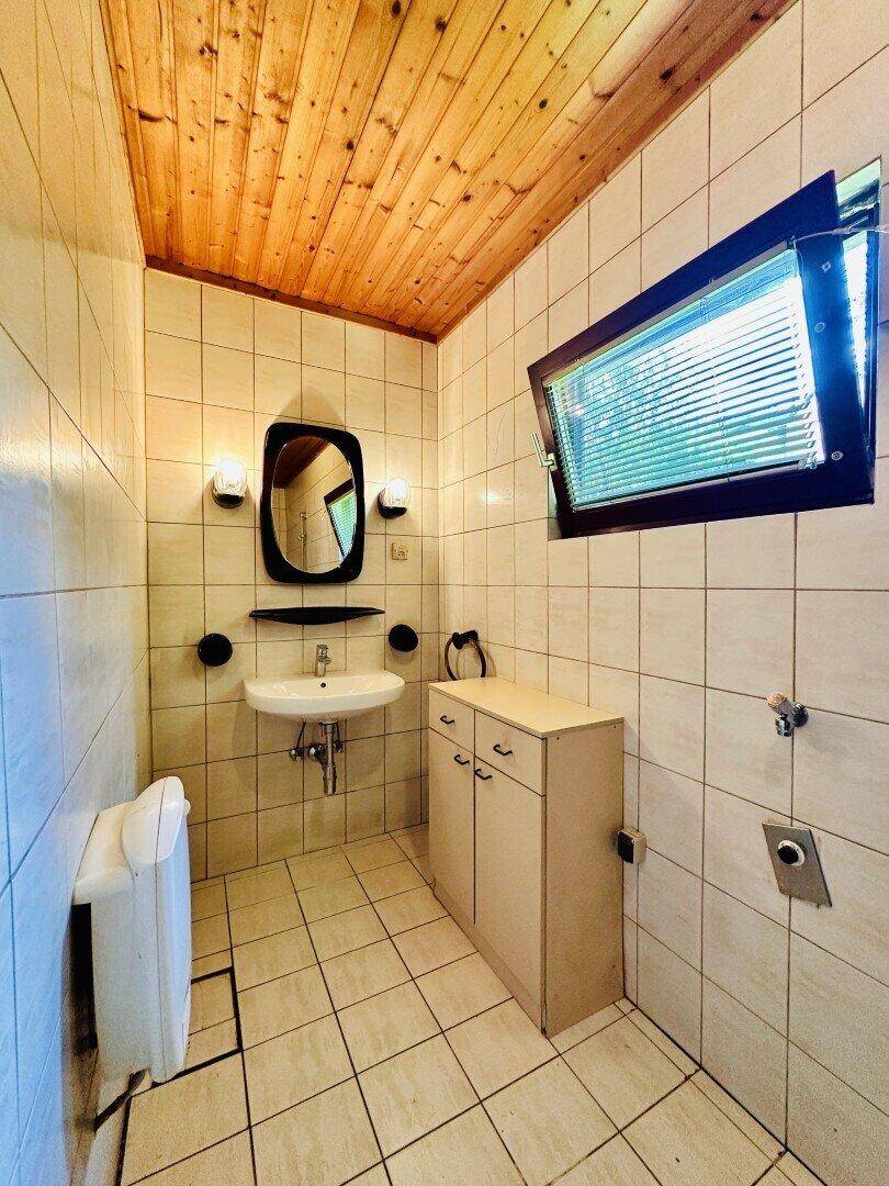 Kleines Badezimmer mit Fliesen, Waschbecken und Holzdecke.