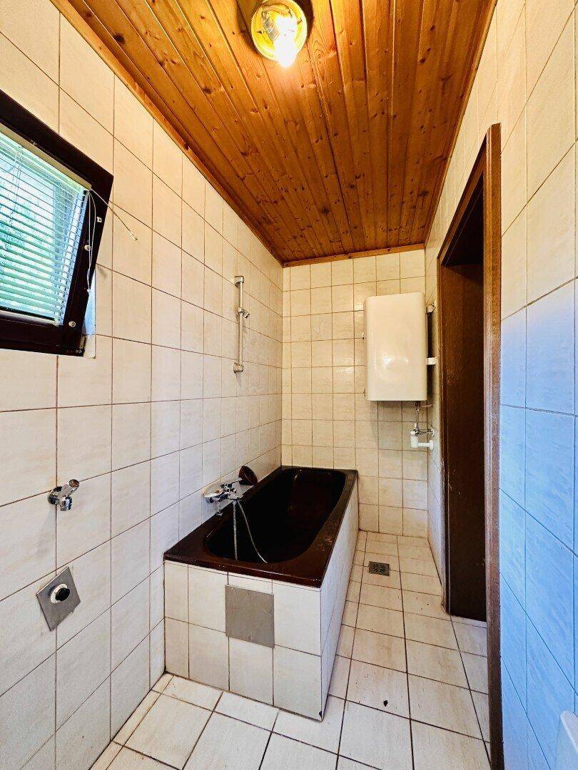 Badezimmer mit Badewanne, Fliesenwänden und Holzdecke im traditionellen Stil.