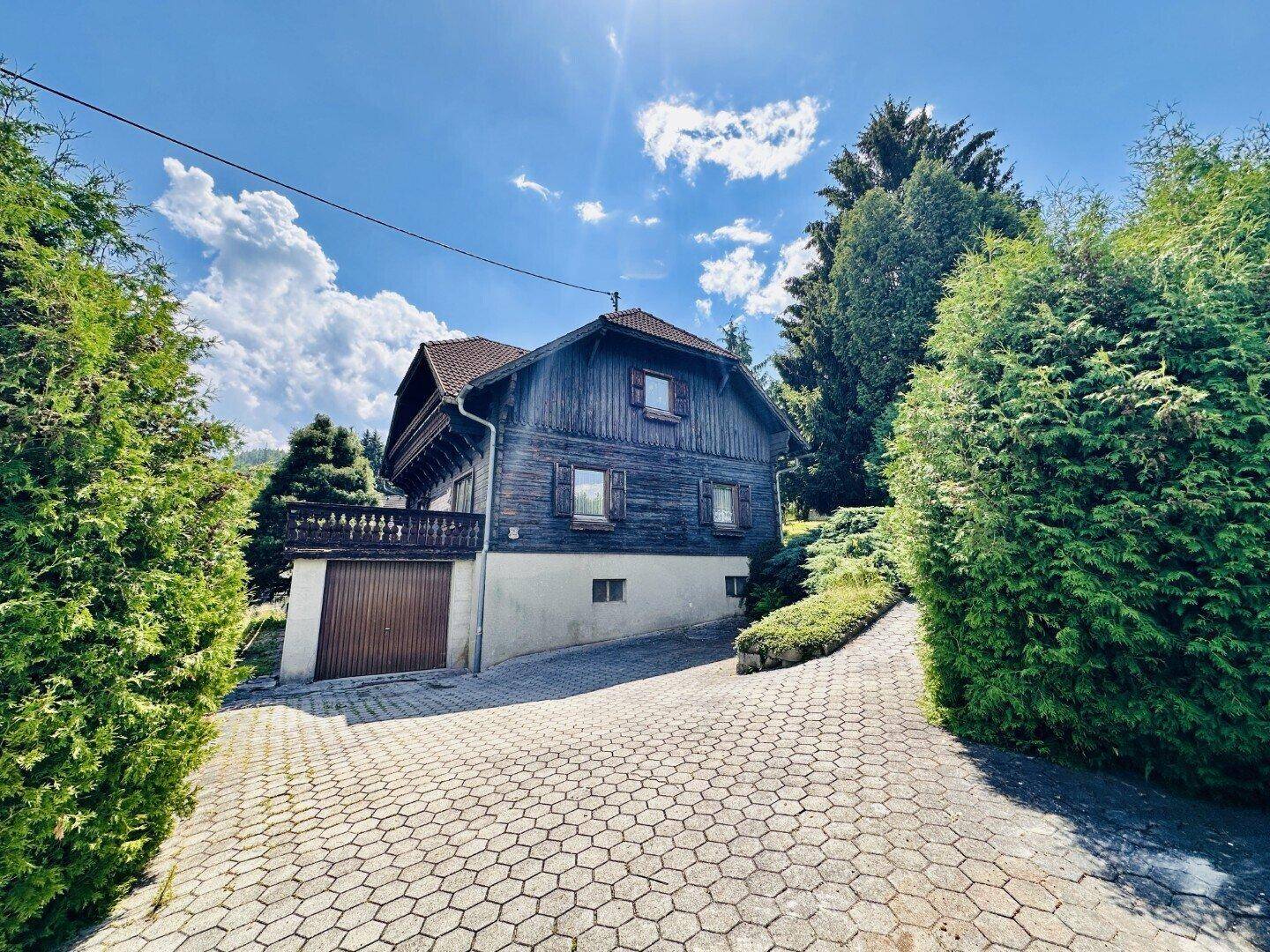 Traditionelles Holzhaus mit gepflasterter Auffahrt und umgebender Natur.