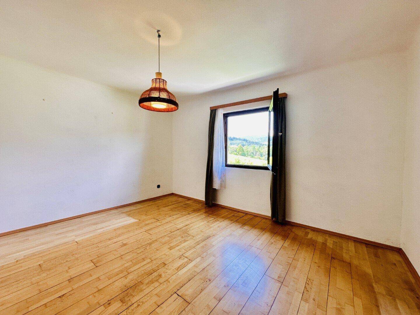 Helles Schlafzimmer mit Holzboden und Fenster mit Blick ins Grüne.