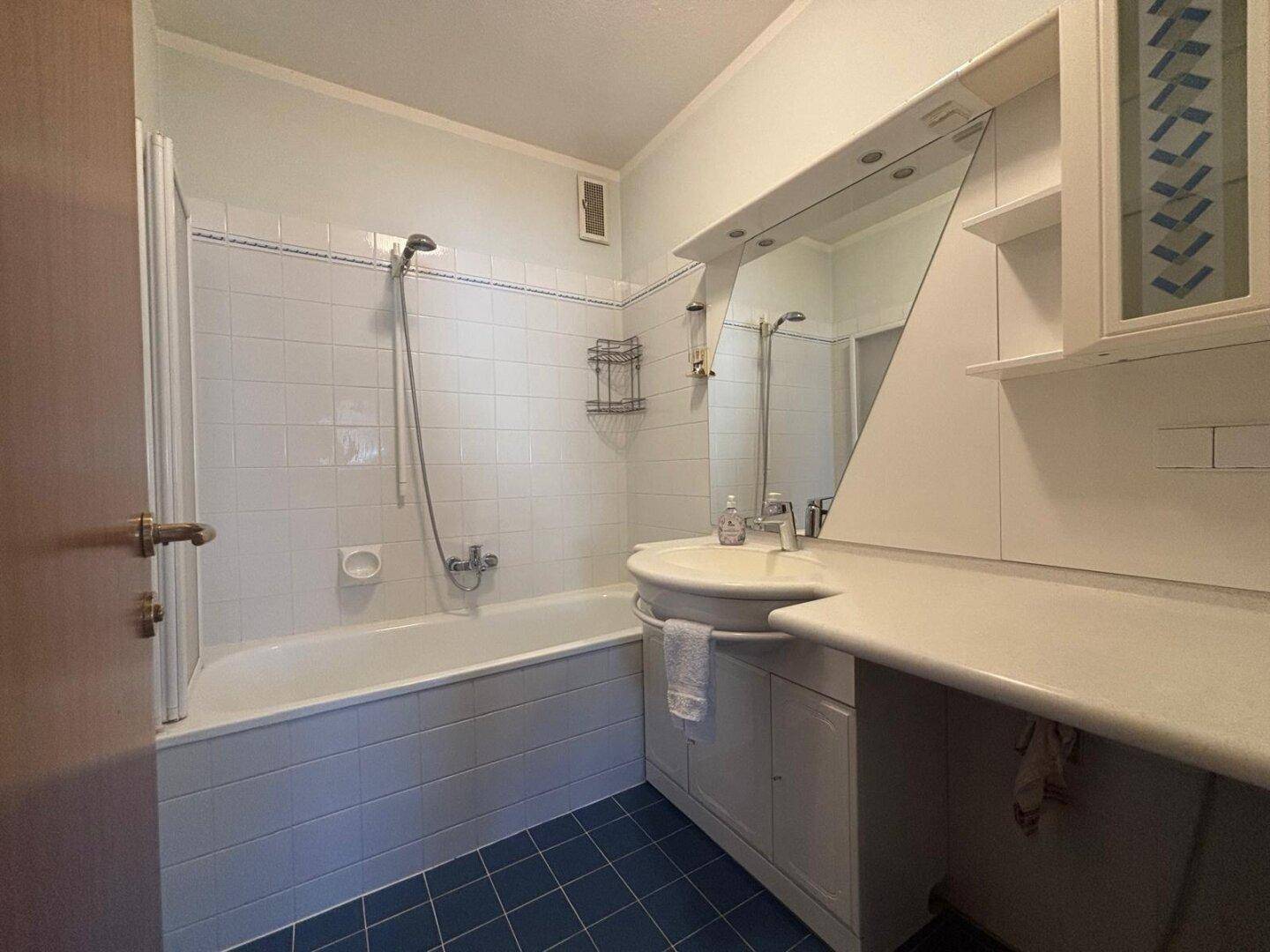 Badezimmer mit Badewanne, Waschbecken und Spiegel, gefliest in Weiß und Blau.