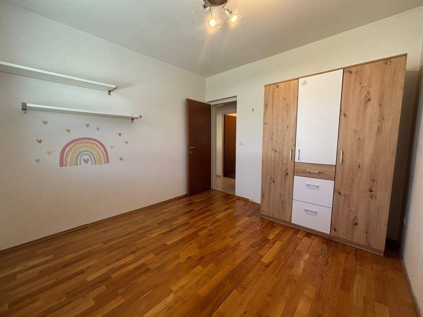 Kinderzimmer mit Holzboden, Kleiderschrank und farbenfrohen Wandstickern.