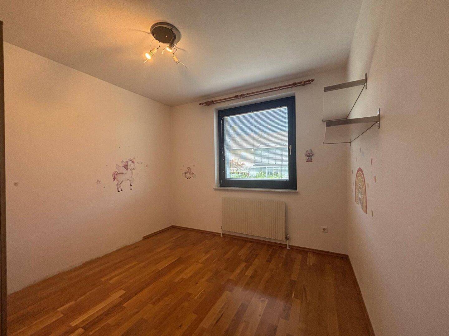 Helles Kinderzimmer mit Holzboden, Fenster und Wanddekorationen.