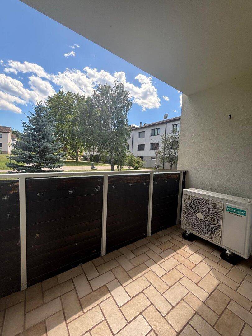 Balkon mit Fliesenboden, Klimaanlage und Blick ins Grüne.