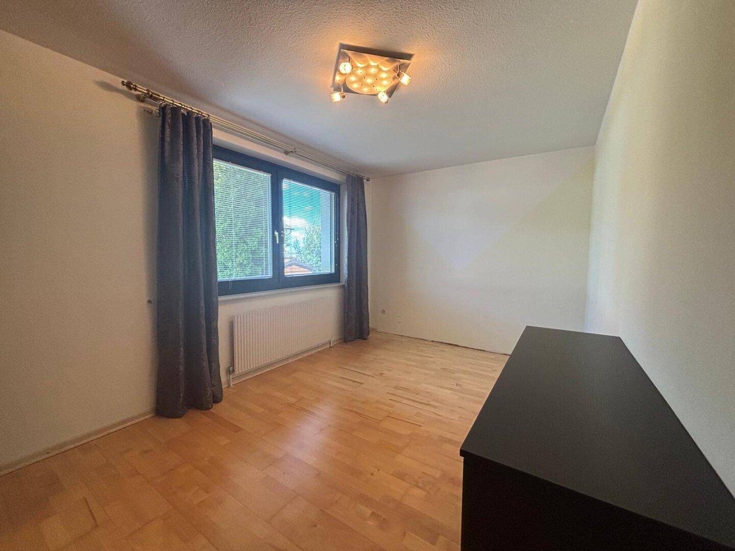 Schlafzimmer mit Holzboden, Fenster mit Vorhängen und Heizkörper.