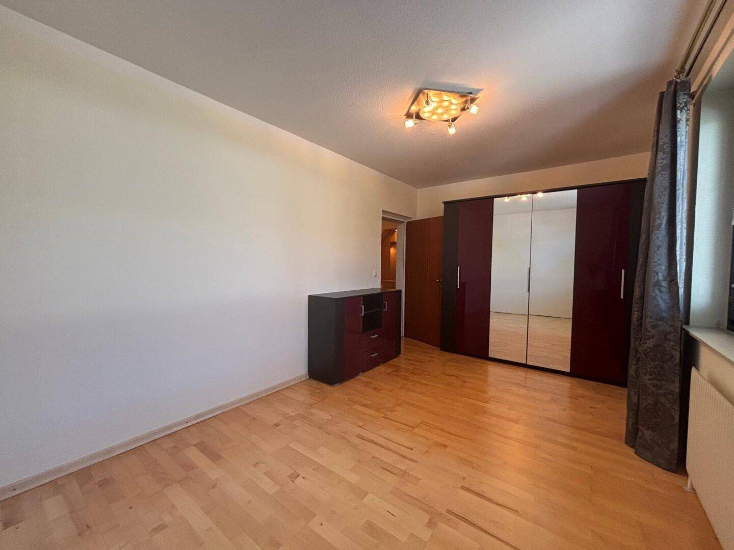 Schlafzimmer mit Holzboden, großem Spiegelschrank und Kommode.