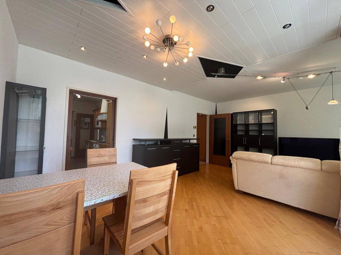Heller Wohn-Essbereich mit Holzboden, modernem Deckenlicht und Essbereich.