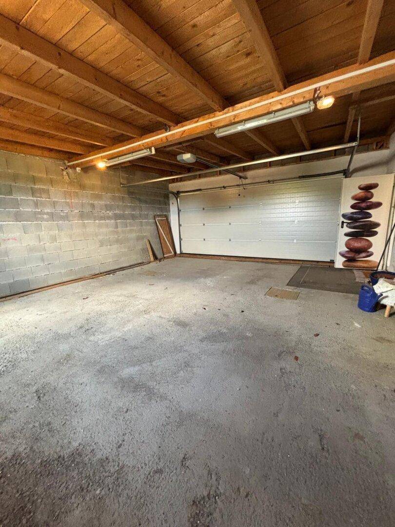 Leere Garage mit Betonboden und Holzbalkendecke, bereit zur Nutzung als Stellplatz.