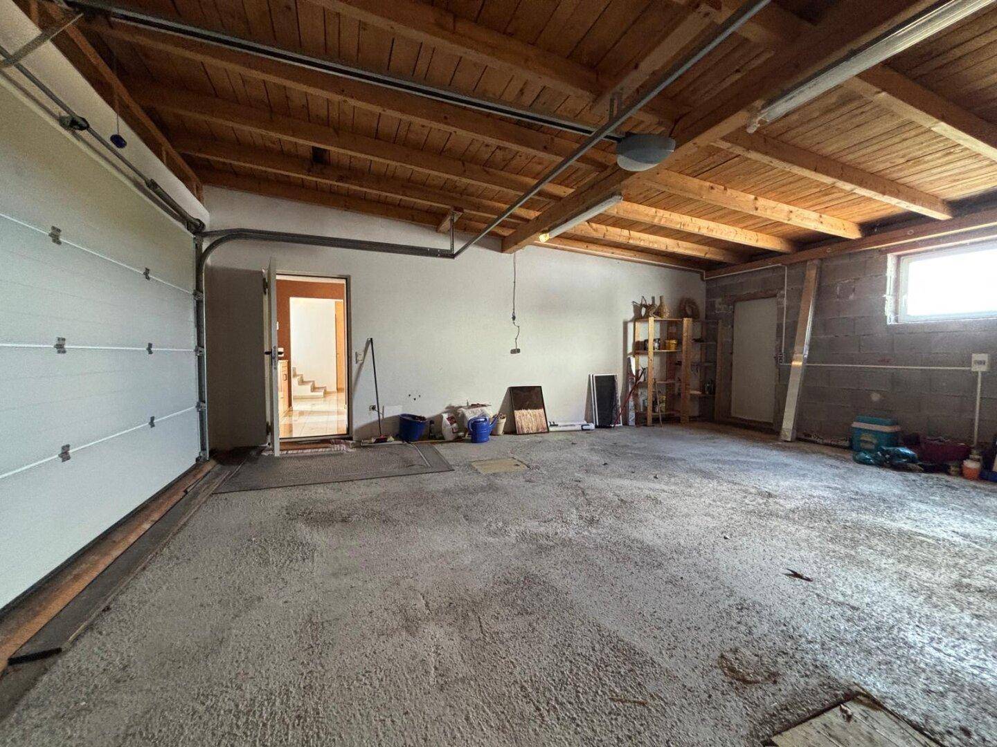 Große Garage mit Betonboden und Holzbalkendecke, ideal für Fahrzeuge und Lagerung.