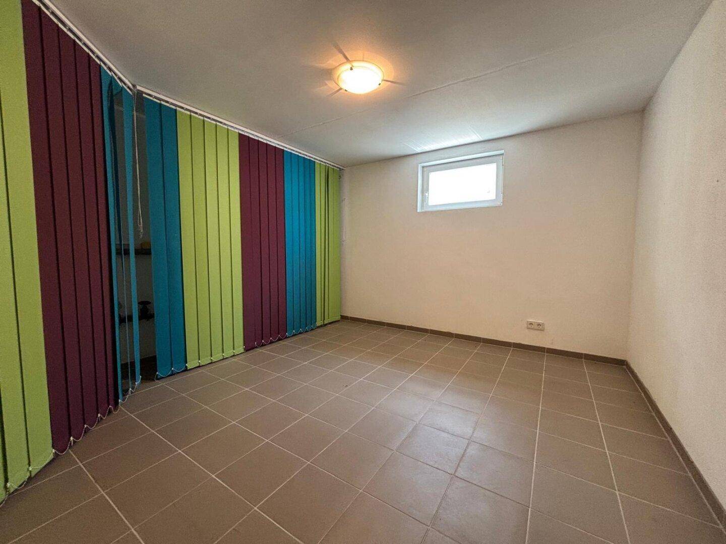 Leerer Raum mit Fliesenboden, Fenster und bunten Vorhängen.