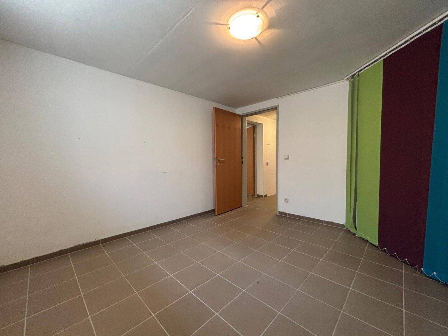 Leerer Raum mit Fliesenboden und bunten Vorhängen, bereit zur individuellen Gestaltung.