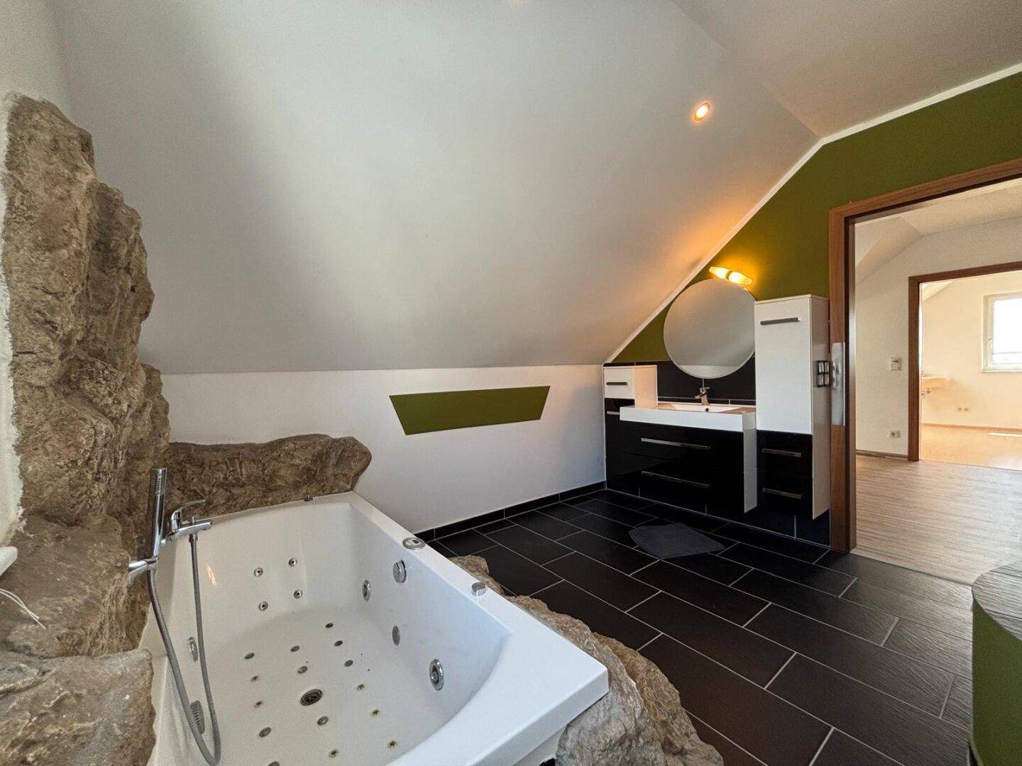 Modernes Badezimmer mit Whirlpool, Doppelwaschbecken und dunklen Fliesen.