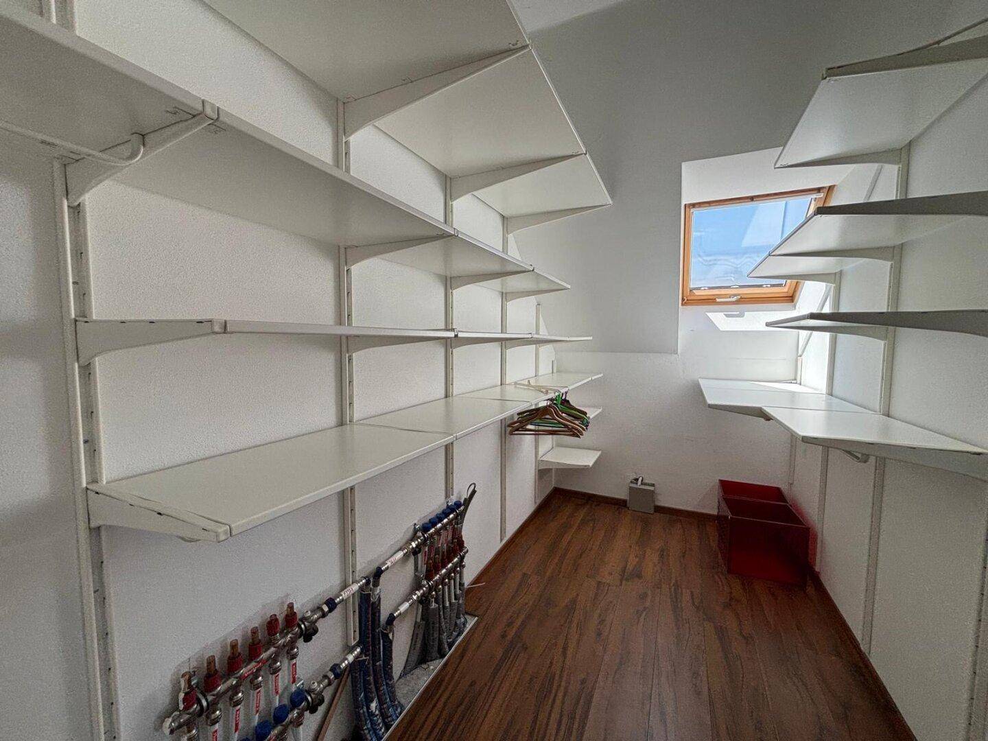 Heller begehbarer Kleiderschrank mit Regalsystem, Dachfenster und Holzboden.