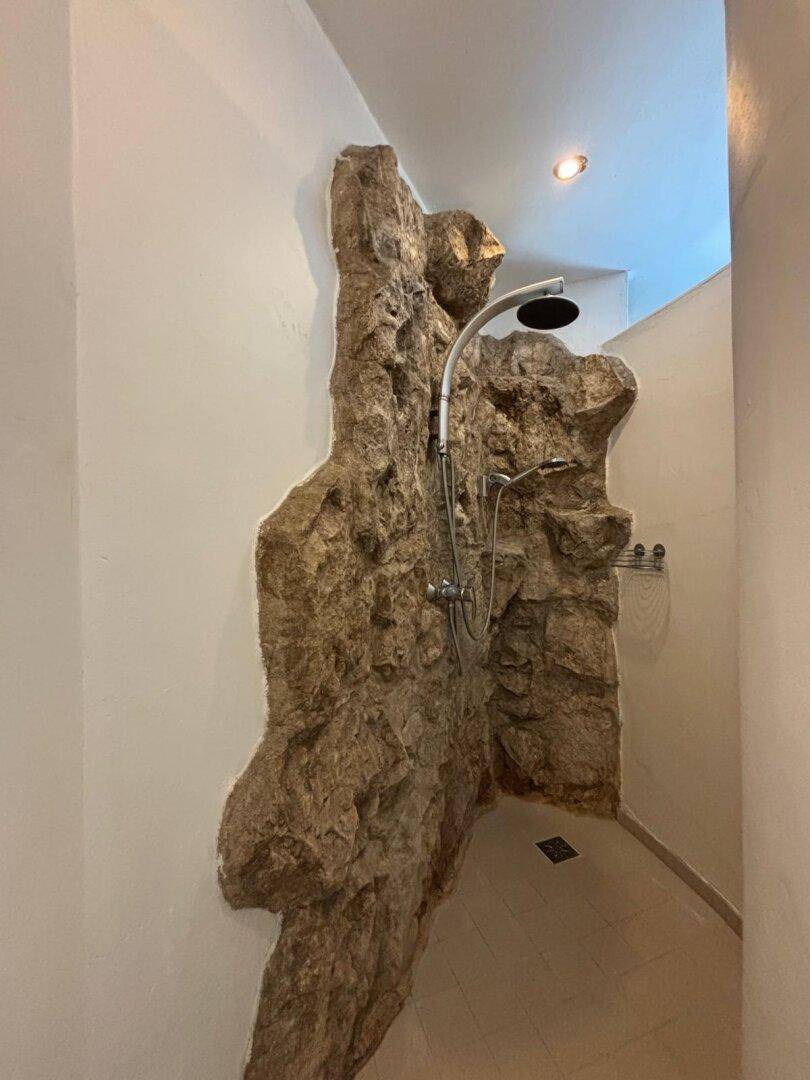 Moderne Dusche mit Natursteinwand und Regenduschkopf.