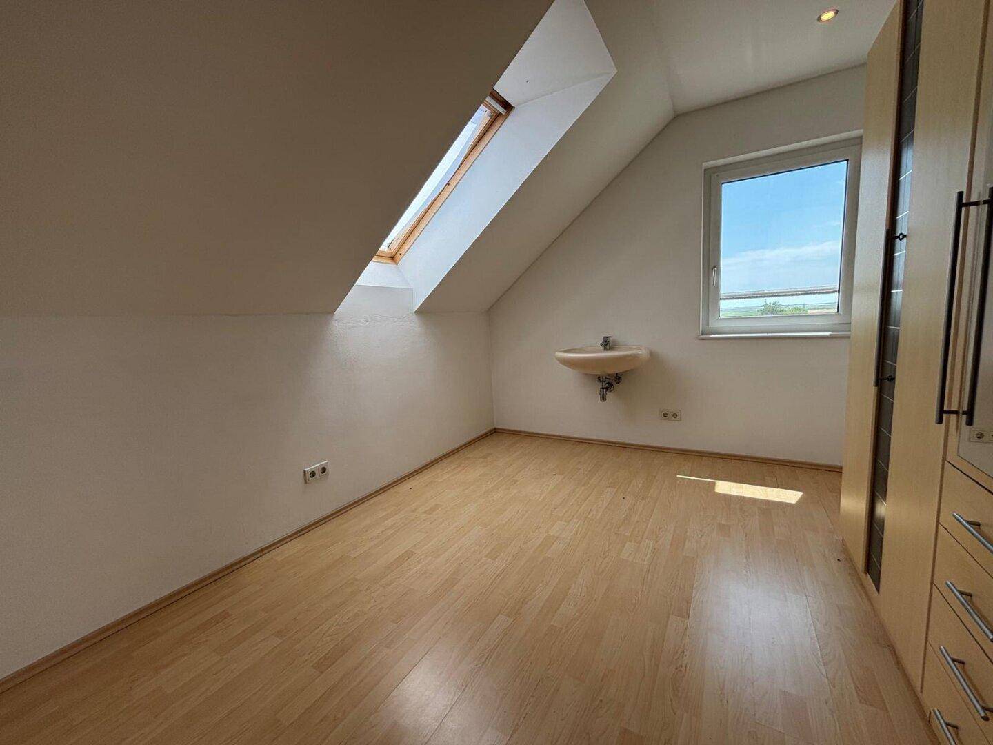 Leeres Zimmer im Dachgeschoss mit Dachfenster, normalem Fenster und Laminatboden.