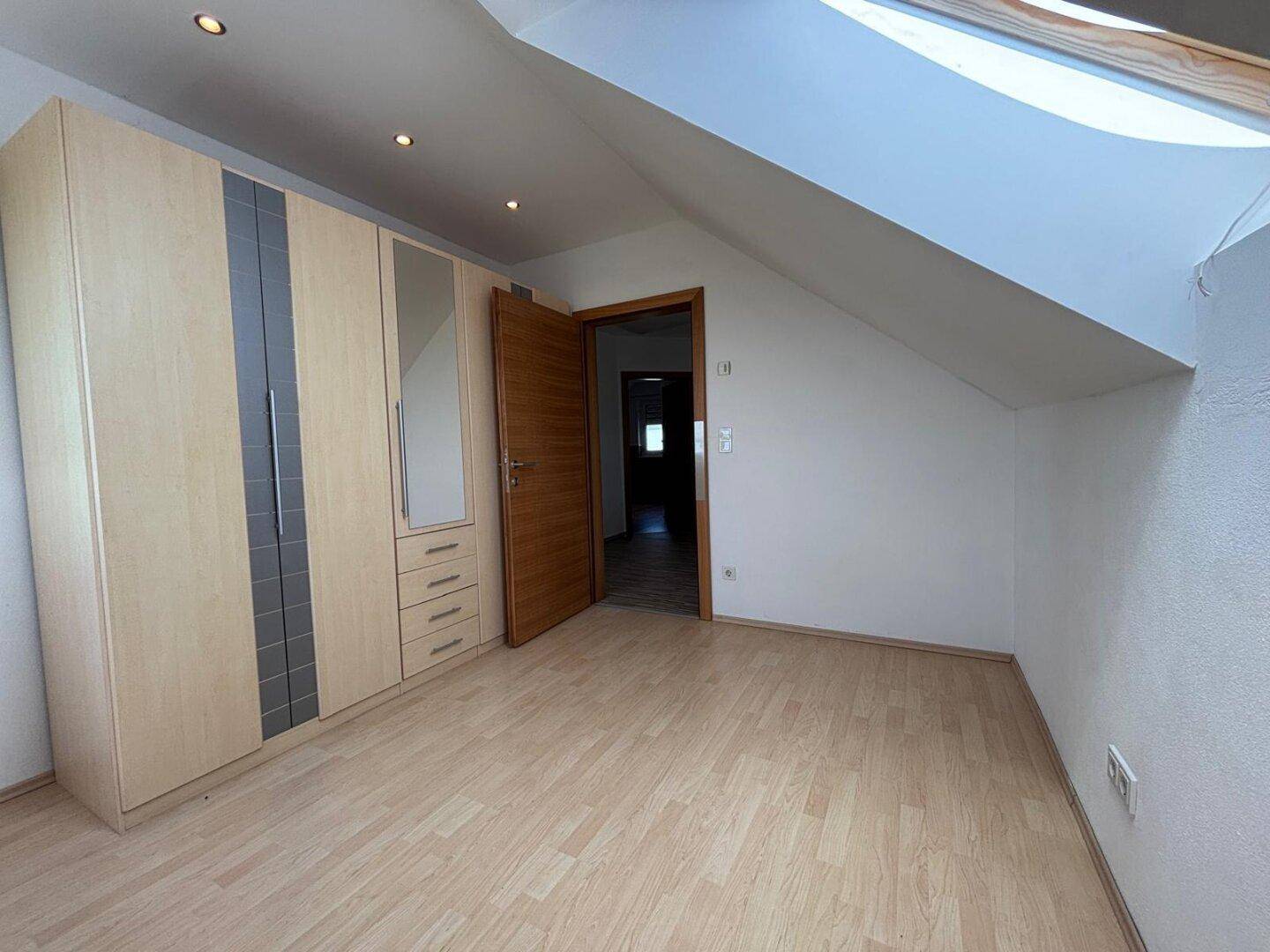 Geräumiges Zimmer im Dachgeschoss mit Einbauschrank, Dachschräge und Laminatboden.