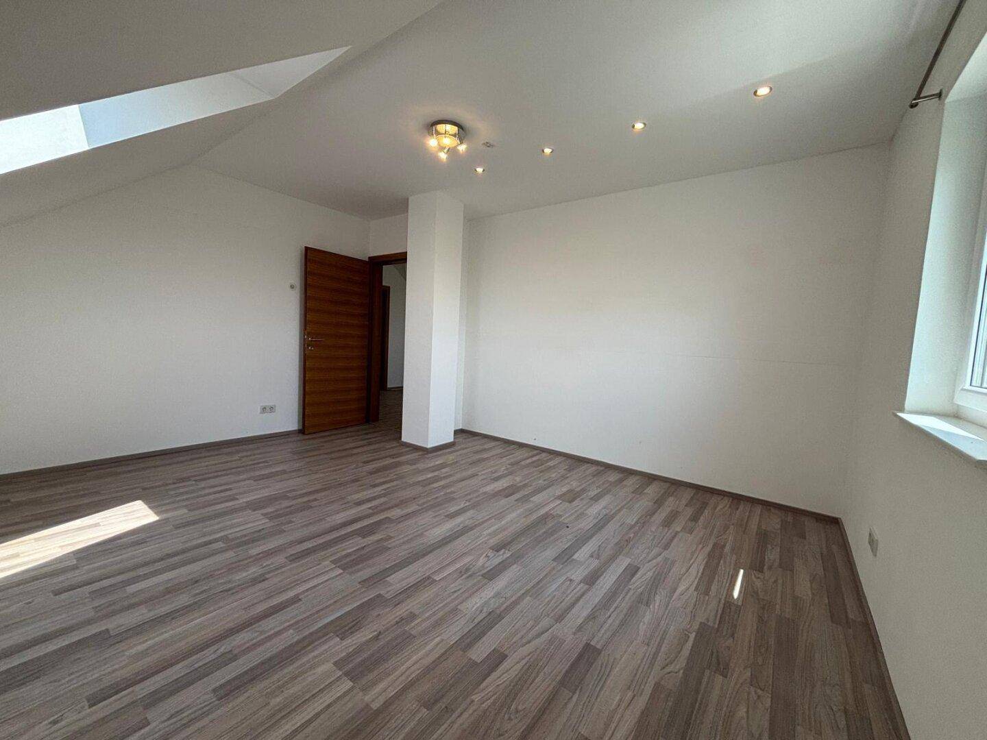 Helles Zimmer im Dachgeschoss mit Holzboden, Dachschräge und Einbaustrahlern.