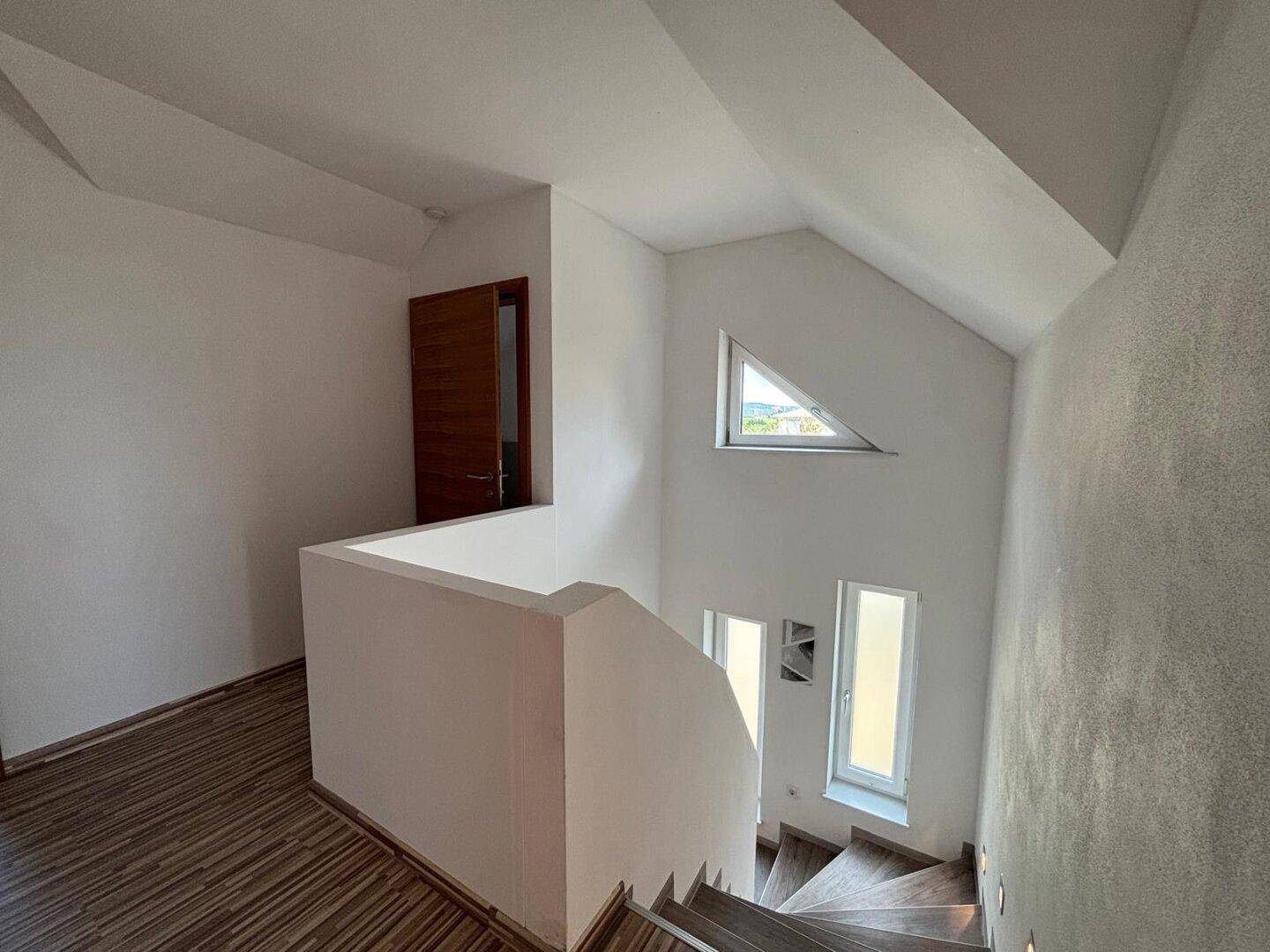 Heller Treppenabsatz mit Laminatboden und besonderen Fensterformen, die viel Licht hereinlassen.