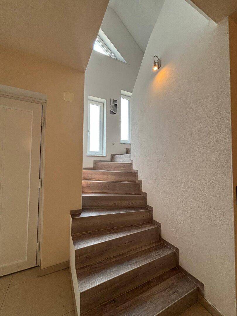 Moderne Holztreppe führt zu den oberen Etagen, mit hohen Decken und natürlichem Lichteinfall.