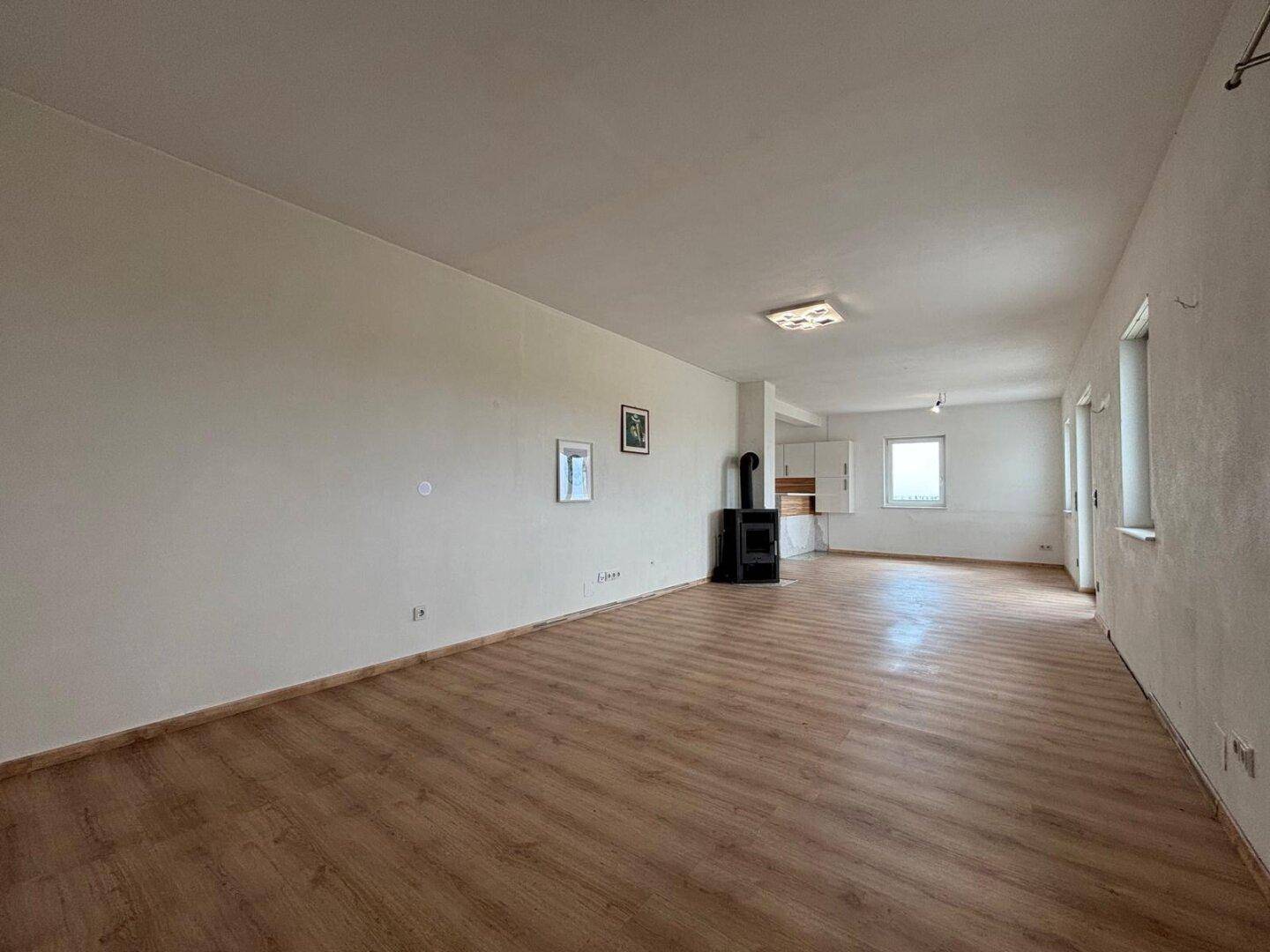 Leeres Wohnzimmer mit Kaminofen, Laminatboden und hellen Wänden, bereit zur individuellen Gestaltung.