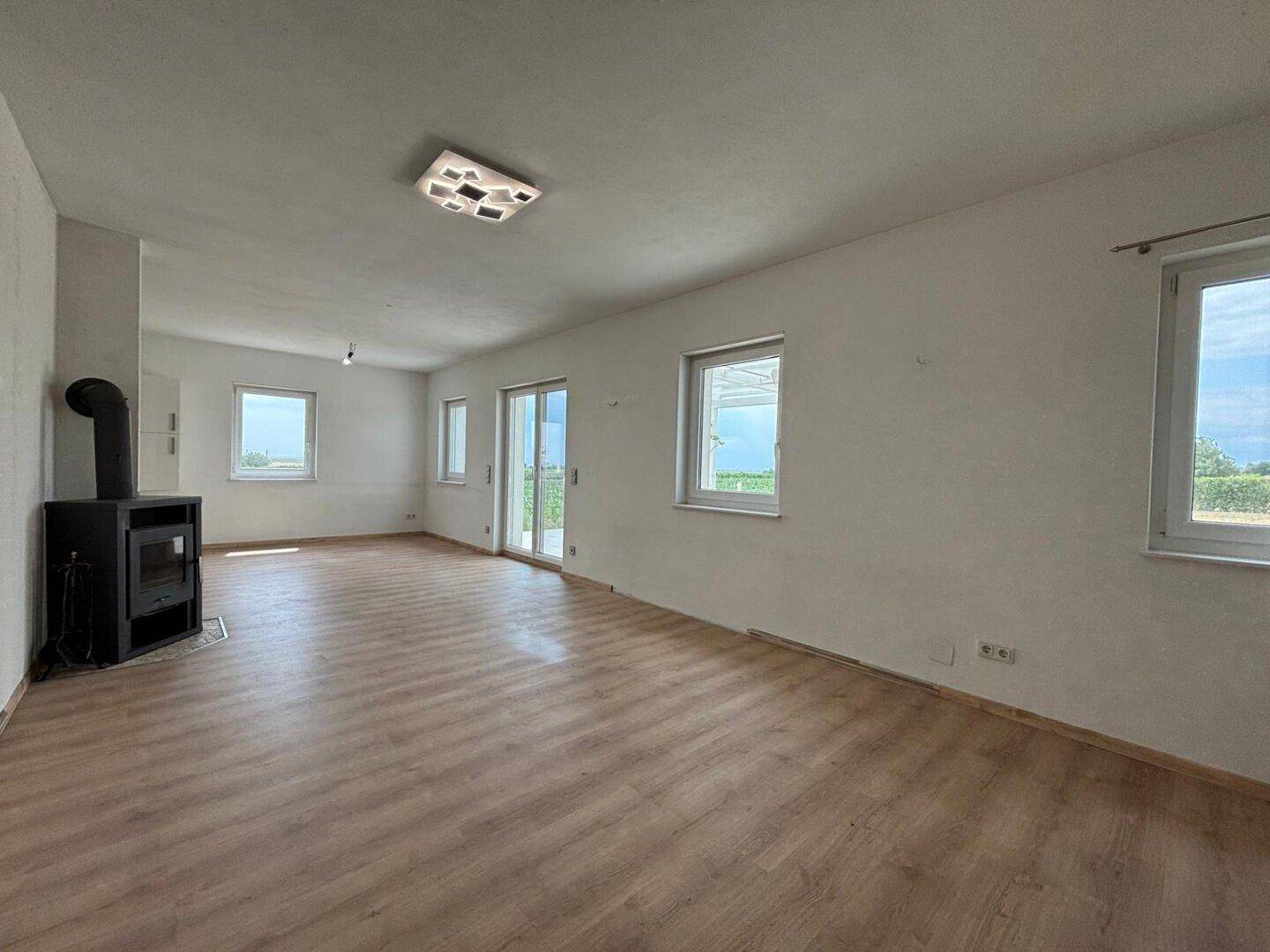 Geräumiges Wohnzimmer mit Kaminofen, Laminatboden und Zugang zur Terrasse, mit Blick ins Grüne.